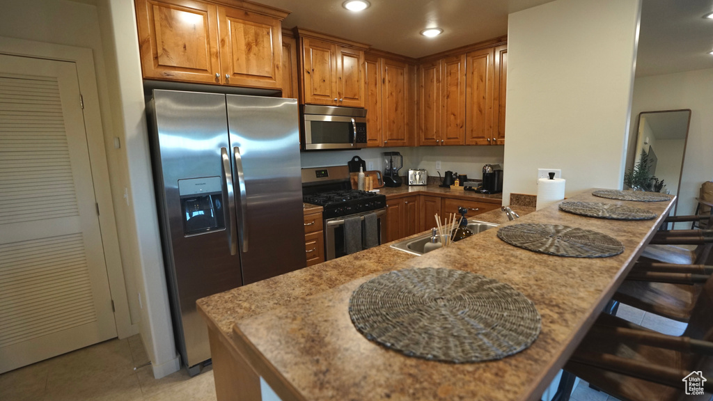 Kitchen with light stone counters, appliances with stainless steel finishes, light tile floors, and a kitchen breakfast bar