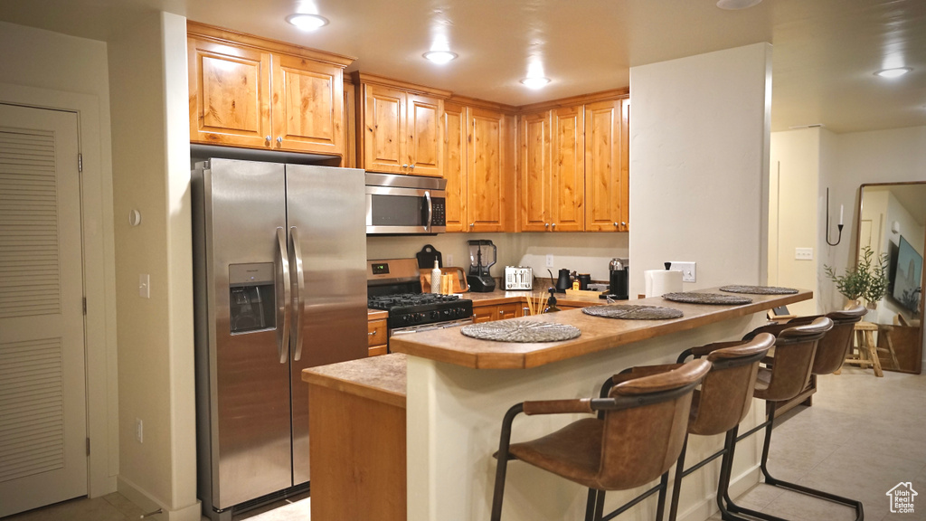 Kitchen with a kitchen bar, appliances with stainless steel finishes, and light tile flooring