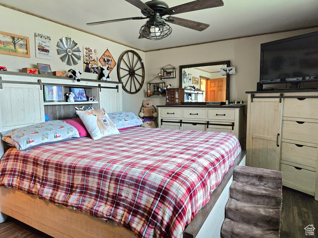 Bedroom featuring ceiling fan, a barn door, and dark wood-type flooring