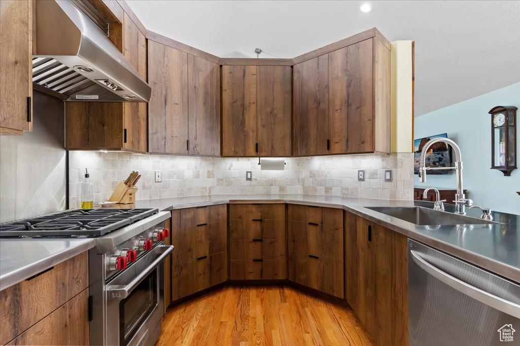 Kitchen featuring backsplash, sink, wall chimney exhaust hood, appliances with stainless steel finishes, and light hardwood / wood-style flooring