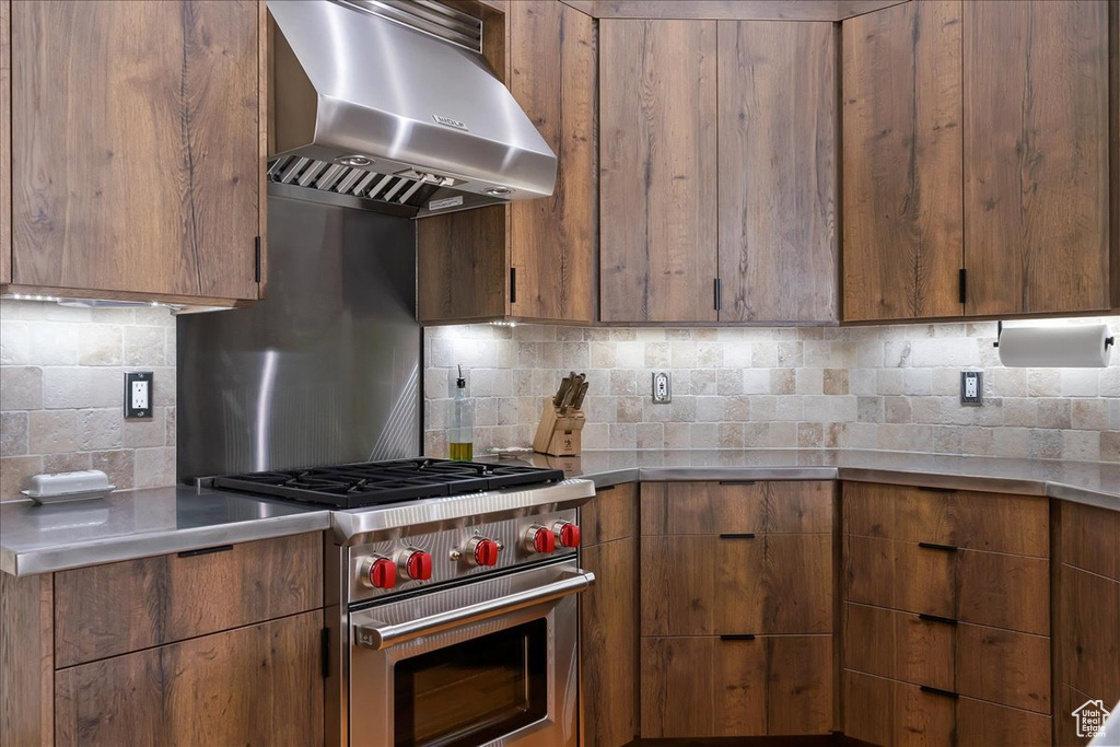 Kitchen featuring backsplash, wall chimney range hood, stainless steel counters, and designer stove