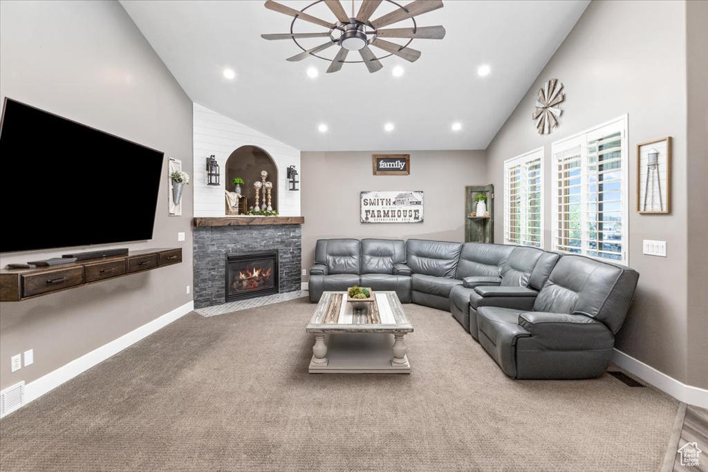 Living room featuring vaulted ceiling, ceiling fan, a stone fireplace, and carpet floors