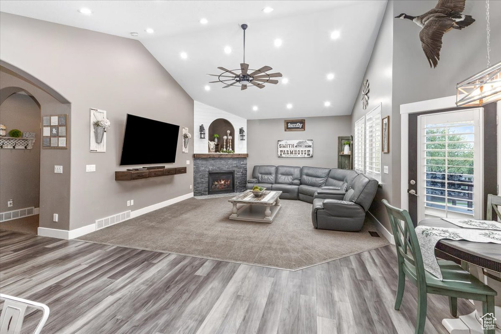Living room featuring dark hardwood / wood-style floors, high vaulted ceiling, ceiling fan, and a stone fireplace