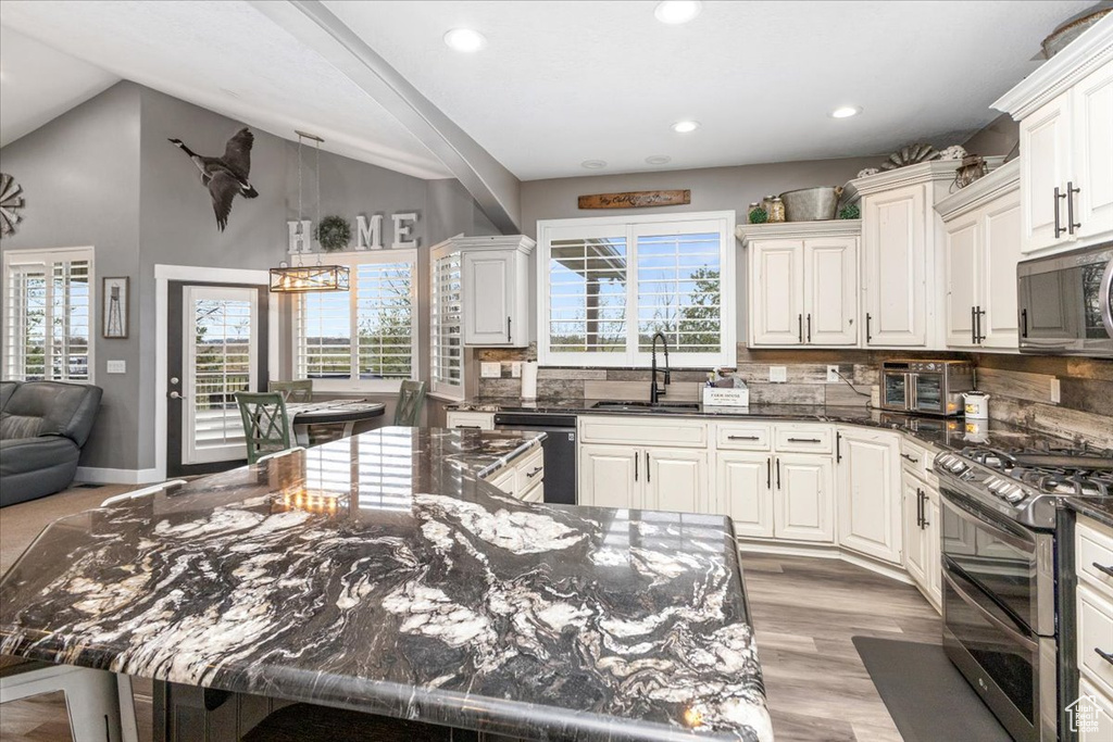 Kitchen featuring high vaulted ceiling, stainless steel appliances, tasteful backsplash, dark stone countertops, and sink