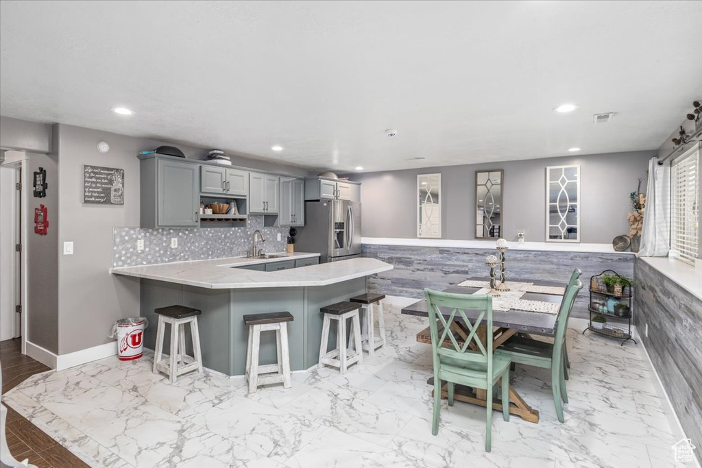 Kitchen with light hardwood / wood-style floors, tasteful backsplash, gray cabinets, kitchen peninsula, and stainless steel refrigerator with ice dispenser