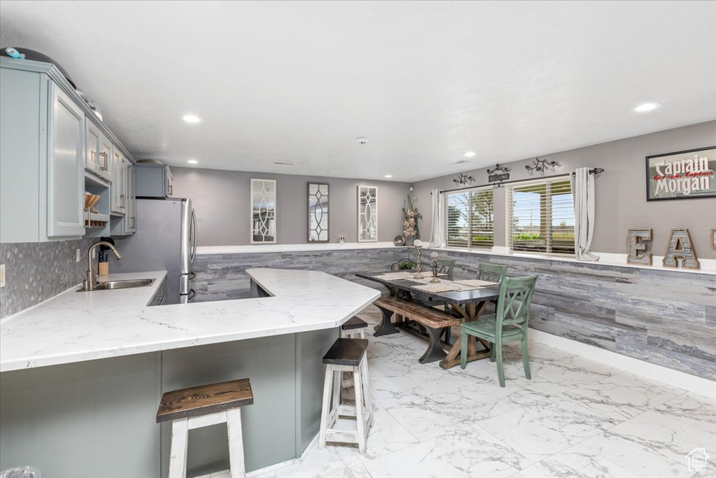 Kitchen featuring light stone countertops, kitchen peninsula, sink, gray cabinetry, and a breakfast bar