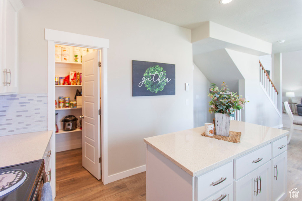 Kitchen featuring a kitchen island, light hardwood / wood-style floors, backsplash, white cabinetry, and stove
