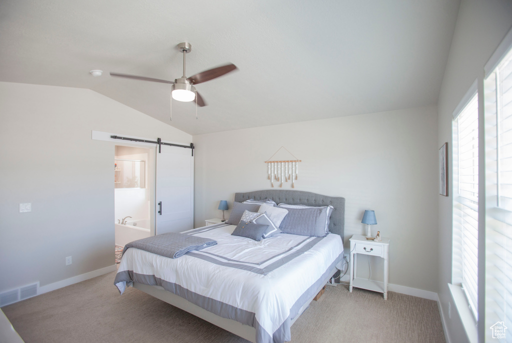 Carpeted bedroom with ensuite bath, a barn door, ceiling fan, and vaulted ceiling