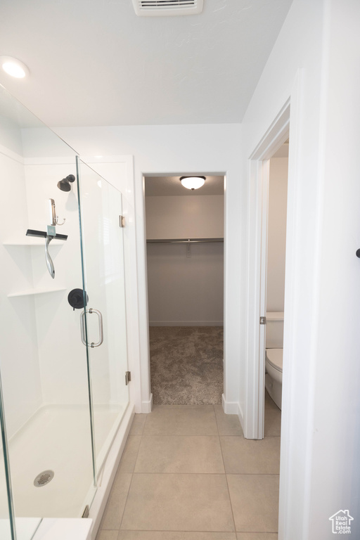 Bathroom with a shower with shower door, toilet, and tile flooring