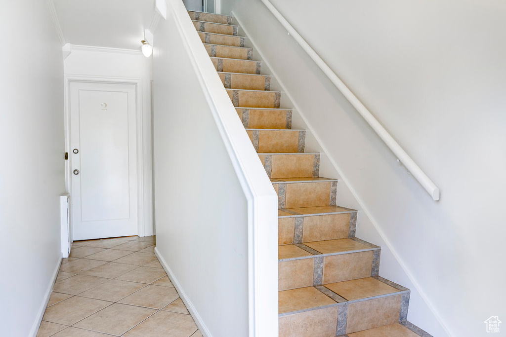 Stairway featuring crown molding and light tile floors