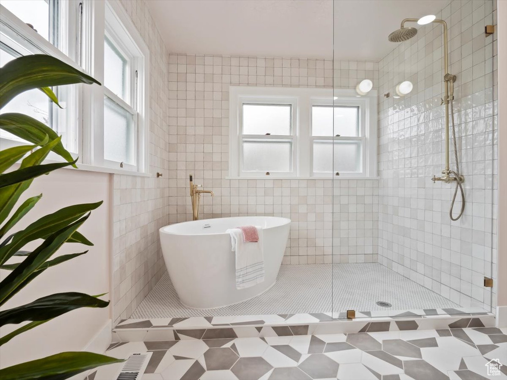 Bathroom featuring a healthy amount of sunlight, tiled shower, tile flooring, and tile walls