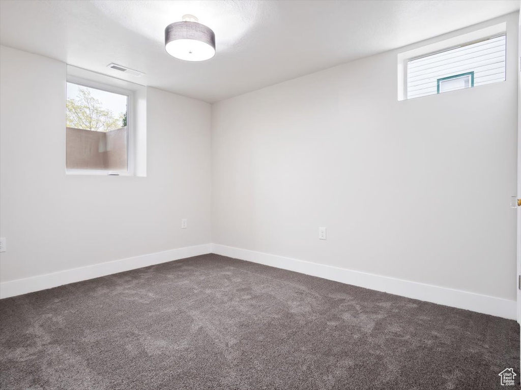 Spare room featuring a wealth of natural light and dark colored carpet