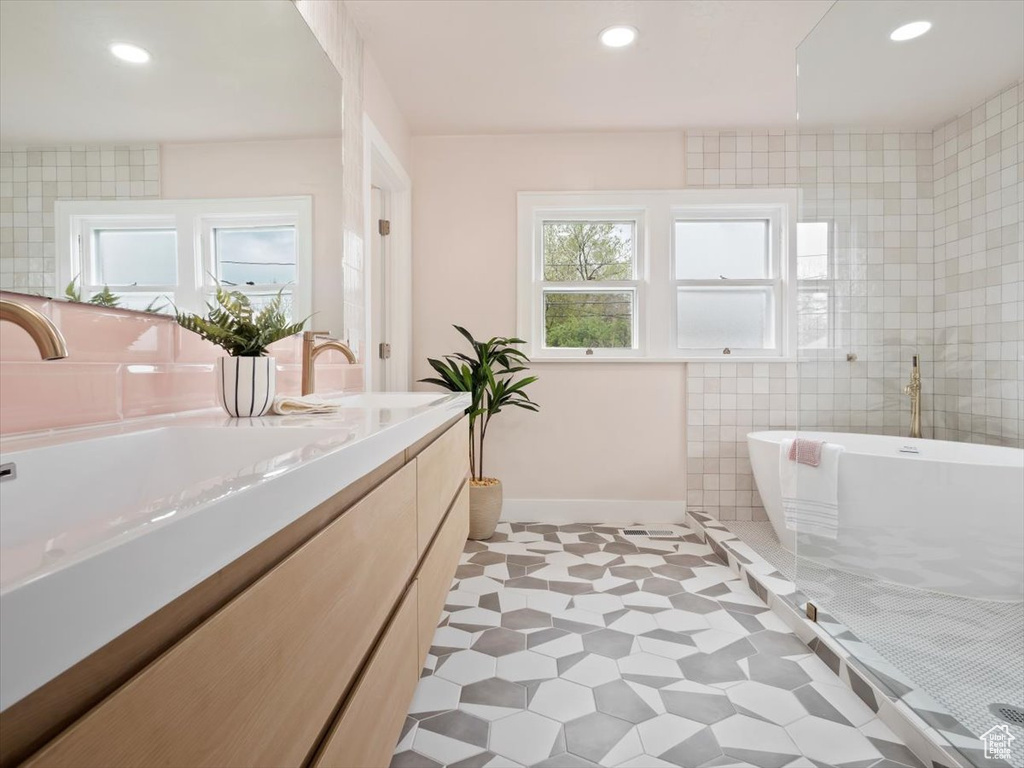 Bathroom with tile walls, independent shower and bath, vanity, and tile flooring