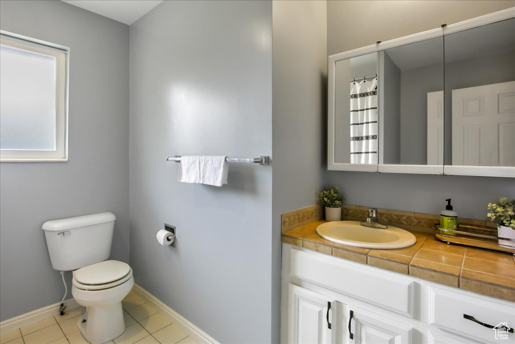 Bathroom with tile floors, oversized vanity, toilet, and a wealth of natural light