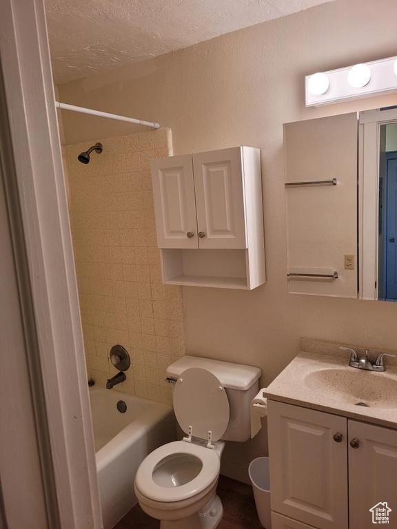 Full bathroom featuring a textured ceiling, vanity, toilet, and tiled shower / bath