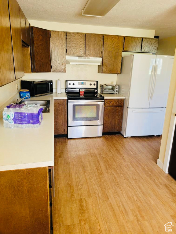 Kitchen with white fridge, range hood, electric range, and light wood-type flooring