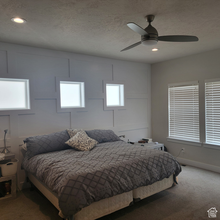 Carpeted bedroom featuring ceiling fan and a textured ceiling