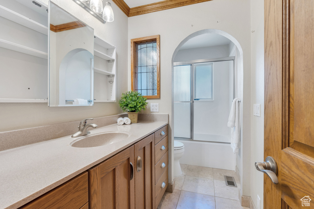 Full bathroom featuring bath / shower combo with glass door, crown molding, toilet, vanity, and tile floors