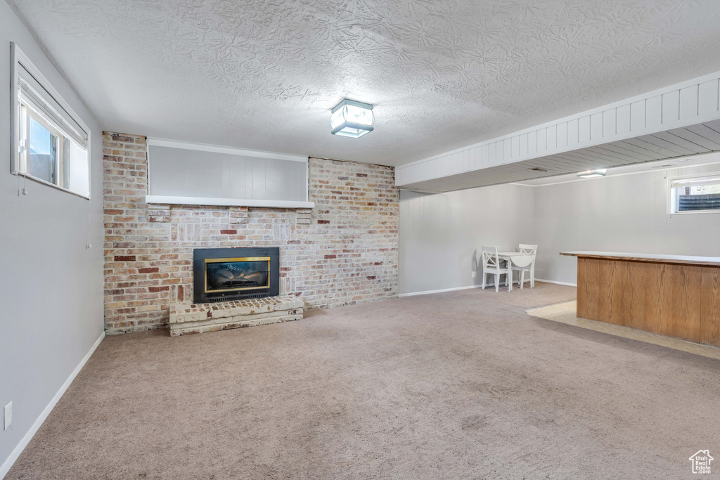 Basement featuring light carpet, a brick fireplace, and a textured ceiling