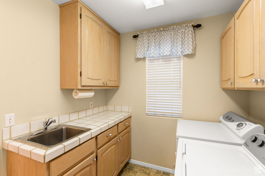 Laundry room with cabinets, sink, washing machine and dryer, and light tile floors