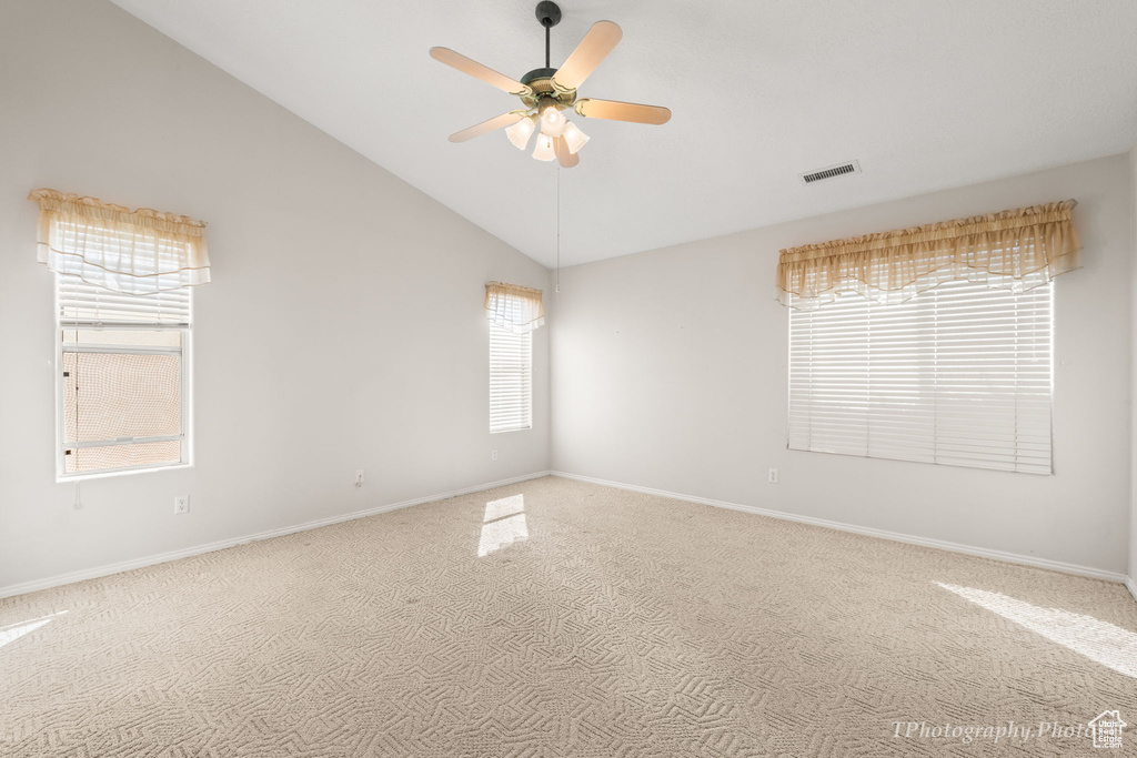 Empty room featuring high vaulted ceiling, plenty of natural light, ceiling fan, and carpet floors