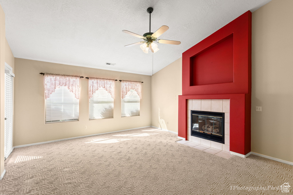Unfurnished living room with lofted ceiling, carpet, ceiling fan, and a tile fireplace