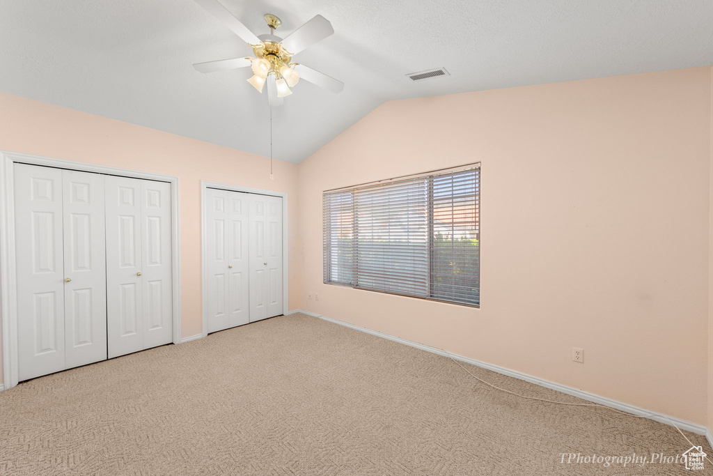 Unfurnished bedroom featuring ceiling fan, carpet floors, vaulted ceiling, and two closets