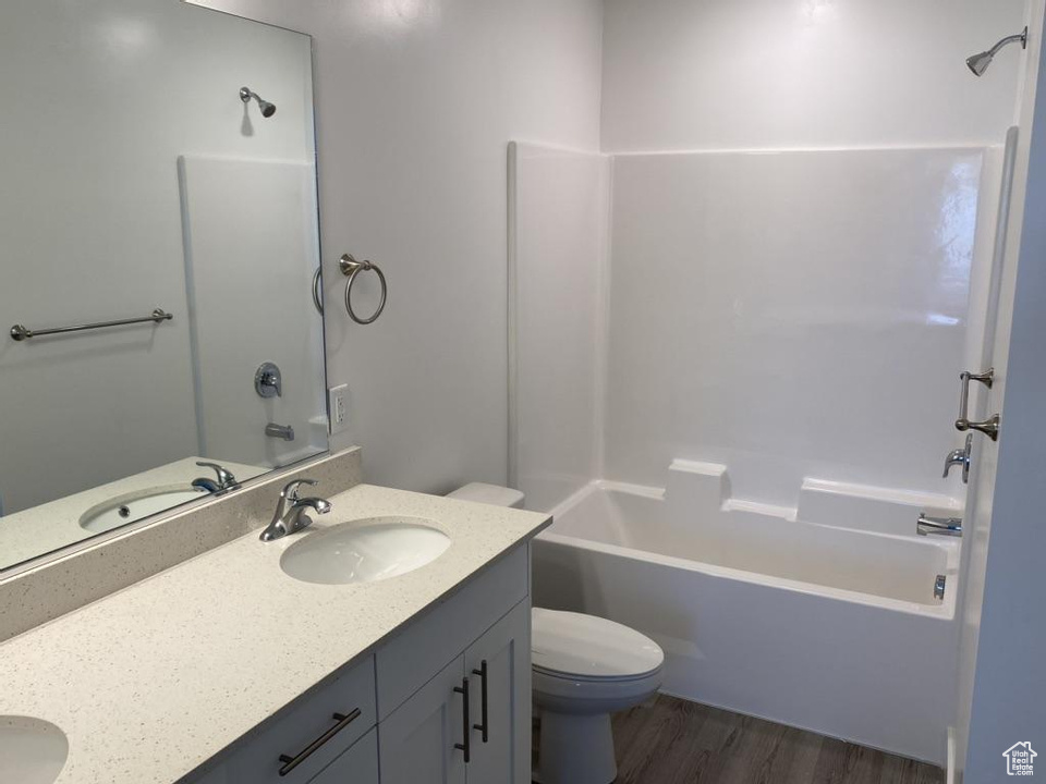 Full bathroom with vanity with extensive cabinet space, bathing tub / shower combination, hardwood / wood-style flooring, dual sinks, and toilet
