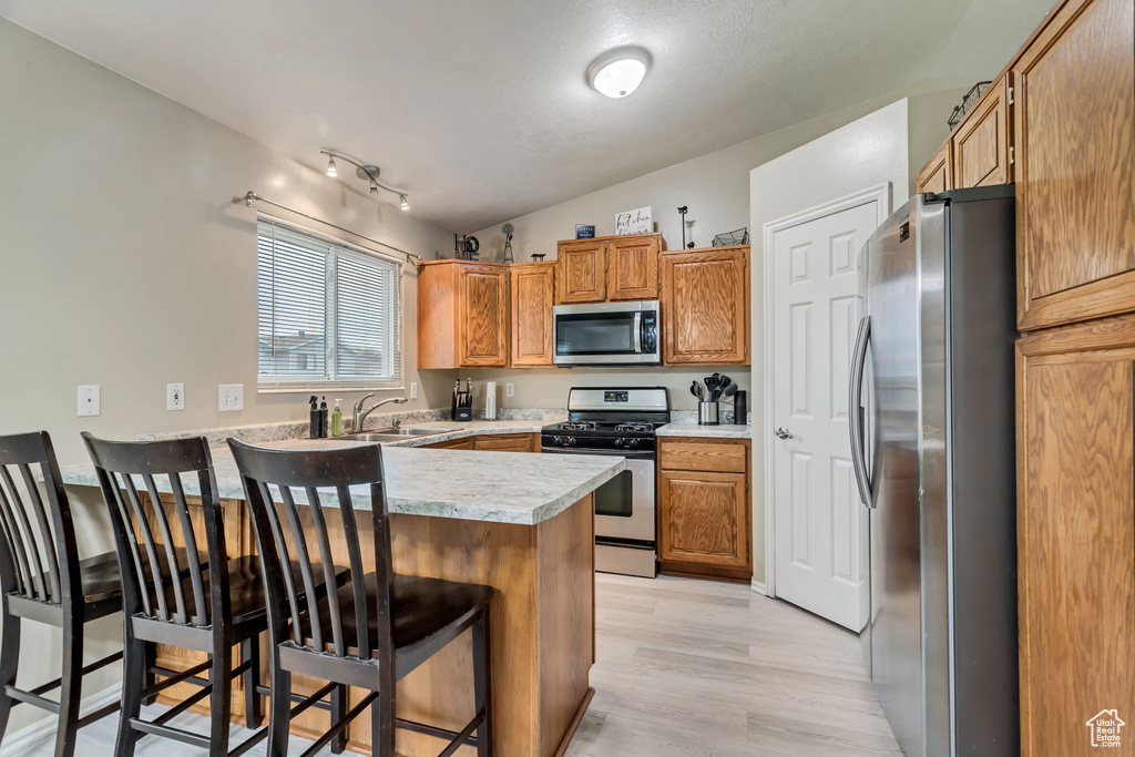 Kitchen with appliances with stainless steel finishes, a breakfast bar area, vaulted ceiling, light hardwood / wood-style floors, and rail lighting