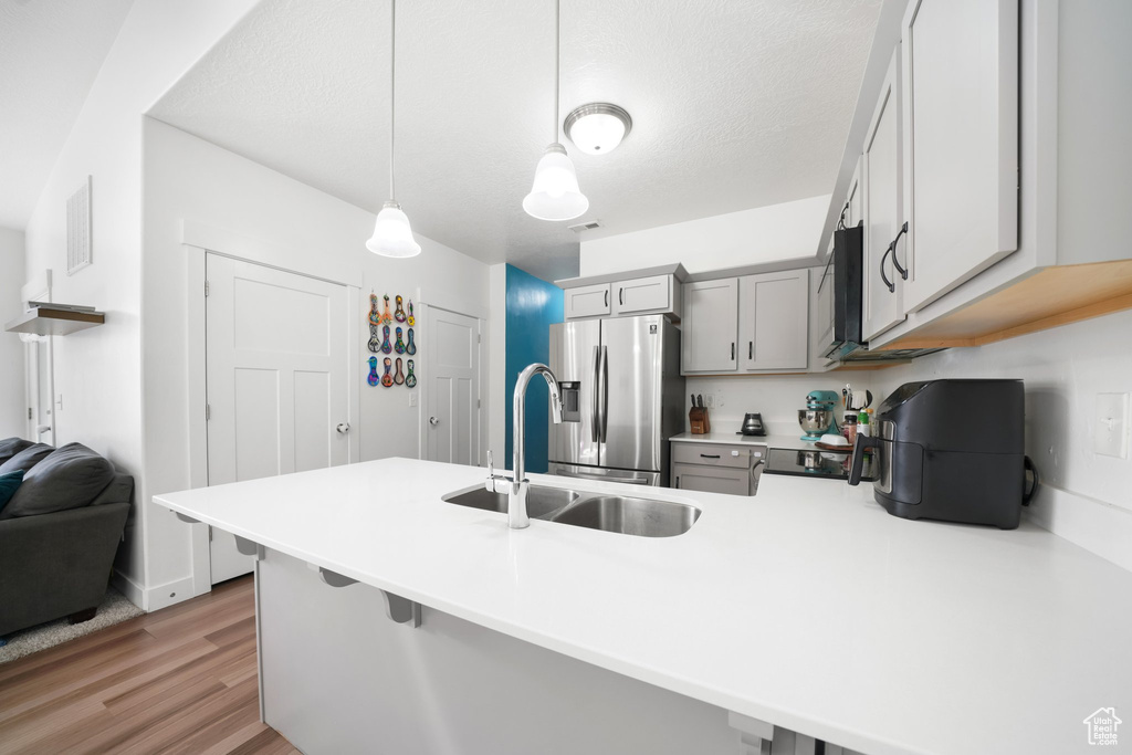 Kitchen featuring sink, light wood-type flooring, decorative light fixtures, stainless steel fridge, and kitchen peninsula
