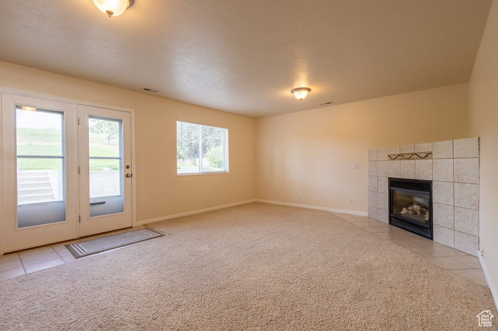 Unfurnished living room featuring light colored carpet and a tiled fireplace