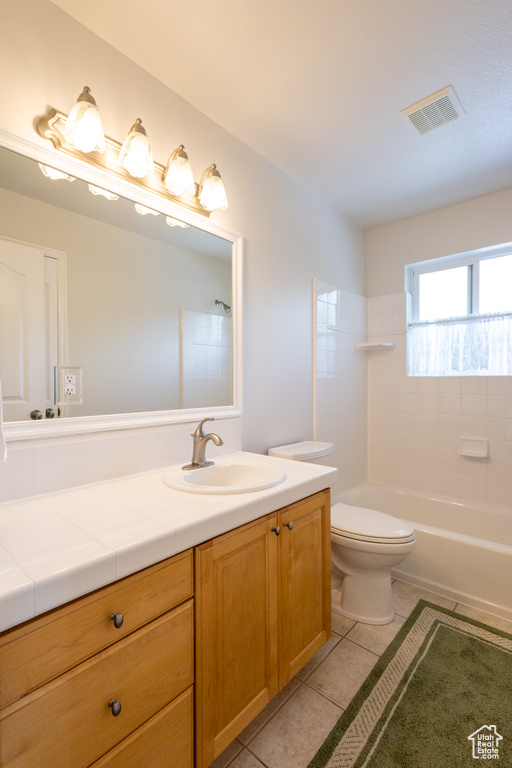 Full bathroom with tiled shower / bath combo, toilet, tile floors, and vanity