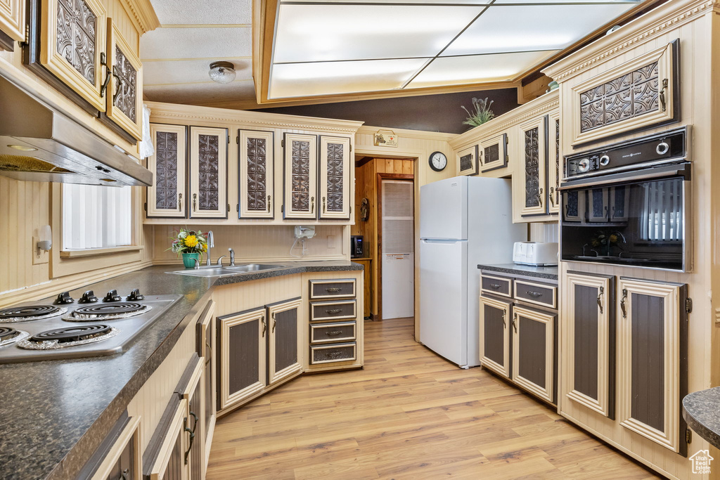 Kitchen featuring cream cabinets, light hardwood / wood-style flooring, white appliances, lofted ceiling, and sink