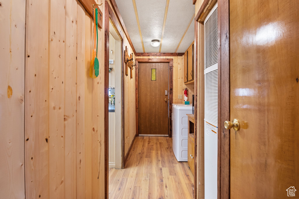 Hallway with washer / clothes dryer, light hardwood / wood-style floors, a textured ceiling, and wooden walls