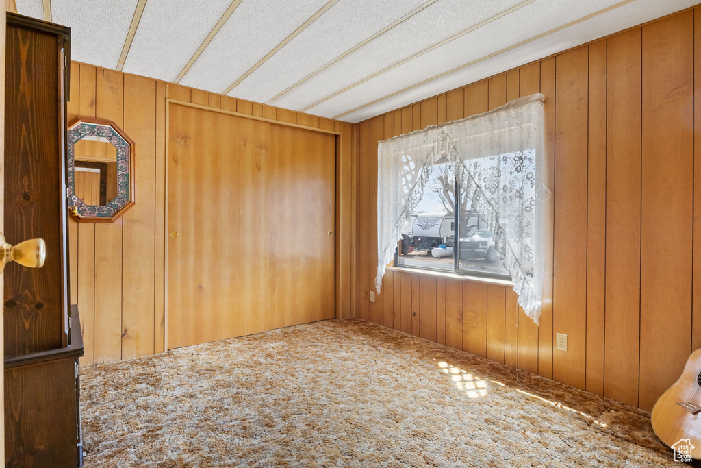 Carpeted spare room with a textured ceiling and wood walls