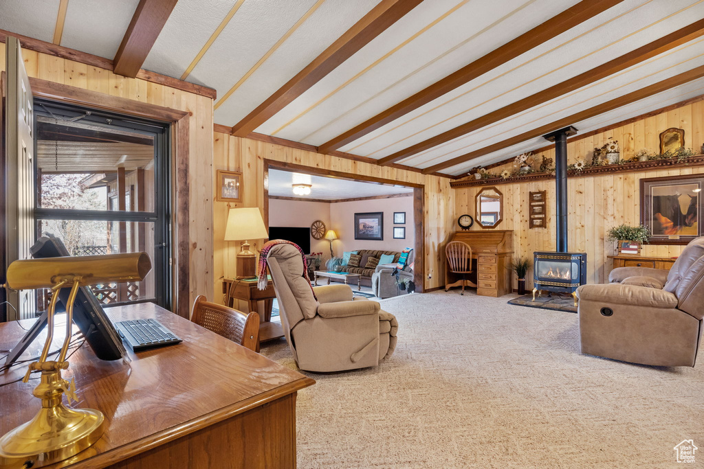 Carpeted living room with lofted ceiling with beams, wood walls, and a wood stove