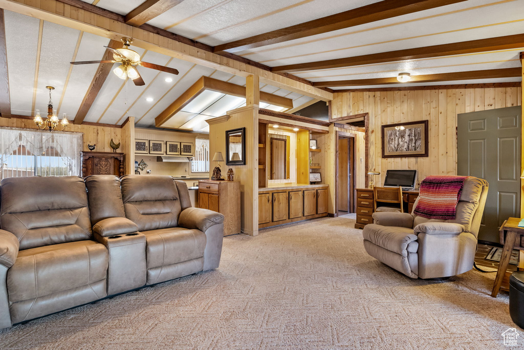 Carpeted living room featuring vaulted ceiling with beams, ceiling fan with notable chandelier, and wooden walls