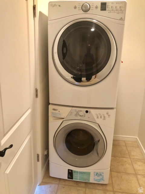 Washroom with stacked washer and clothes dryer and light tile floors
