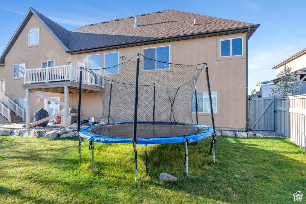 Rear view of property featuring a yard, a wooden deck, and a trampoline
