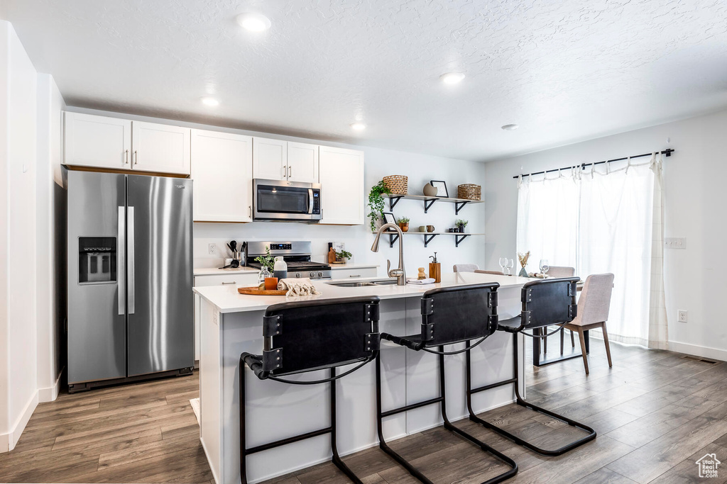 Kitchen with a kitchen bar, white cabinetry, hardwood / wood-style floors, stainless steel appliances, and a center island with sink