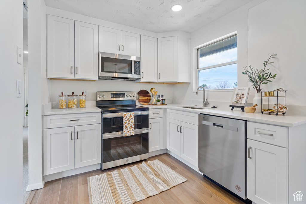 Kitchen with sink, appliances with stainless steel finishes, light hardwood / wood-style floors, and white cabinetry