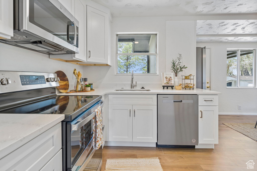 Kitchen with white cabinets, sink, light wood-type flooring, and stainless steel appliances