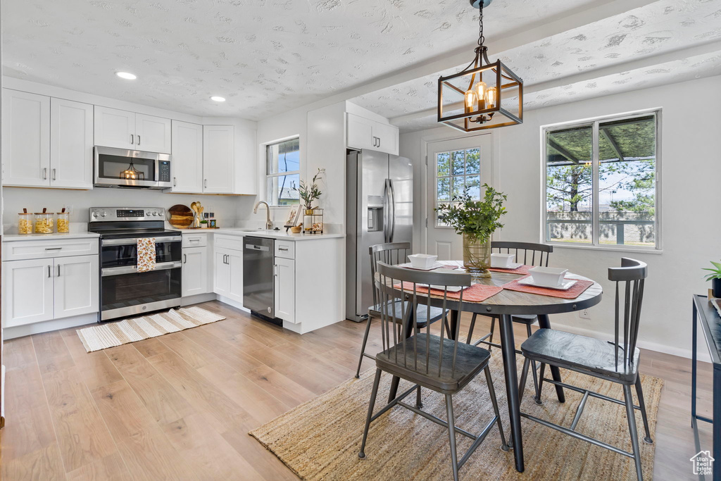 Kitchen with appliances with stainless steel finishes, hanging light fixtures, white cabinets, and light hardwood / wood-style flooring