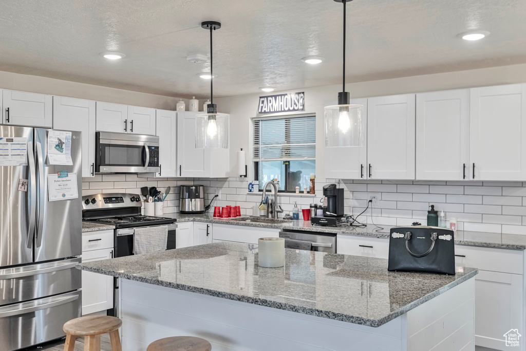 Kitchen with appliances with stainless steel finishes, light stone counters, white cabinets, and hanging light fixtures