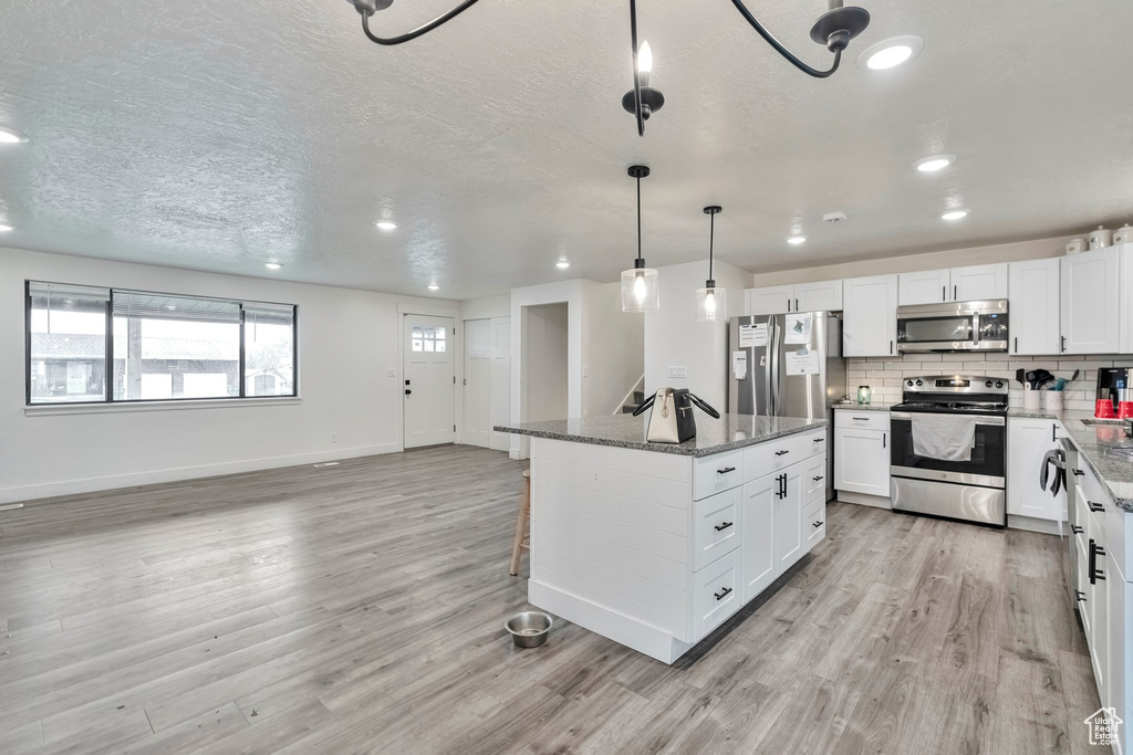 Kitchen with dark stone countertops, stainless steel appliances, and light wood-type flooring