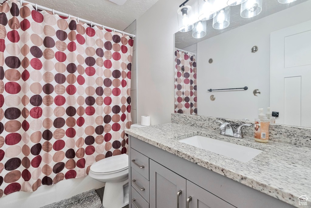 Full bathroom featuring a textured ceiling, oversized vanity, toilet, and shower / bath combo with shower curtain
