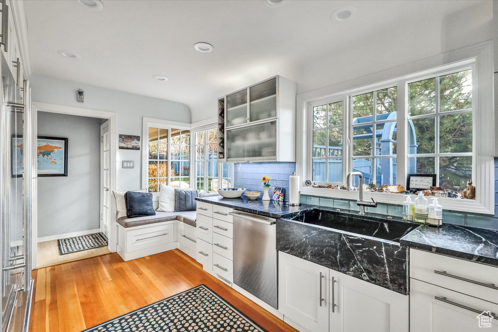 Kitchen featuring white cabinets, light wood-type flooring, backsplash, stainless steel dishwasher, and dark stone counters