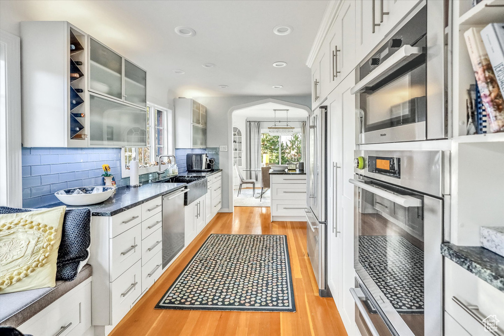 Kitchen with white cabinets, light hardwood / wood-style flooring, sink, tasteful backsplash, and dishwasher