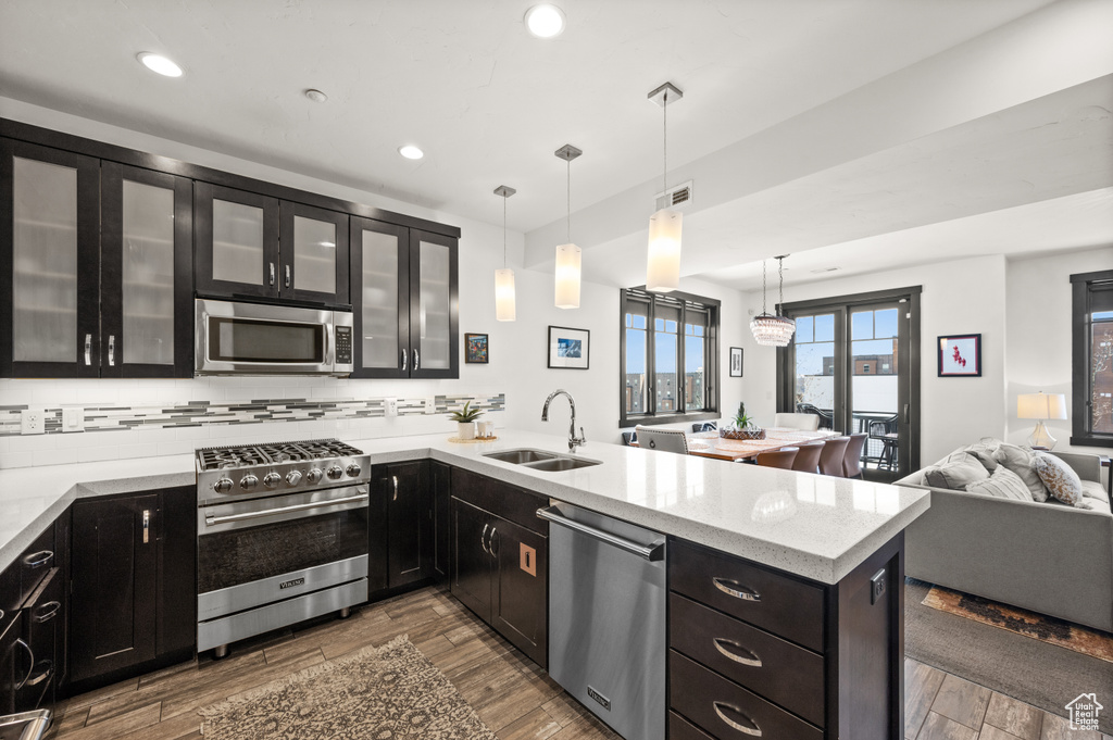 Kitchen featuring decorative light fixtures, appliances with stainless steel finishes, wood-type flooring, tasteful backsplash, and sink