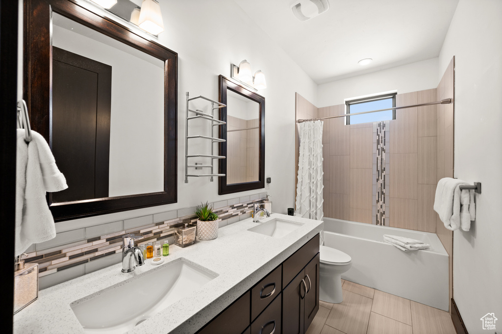 Full bathroom with dual bowl vanity, shower / bathtub combination with curtain, backsplash, toilet, and tile floors